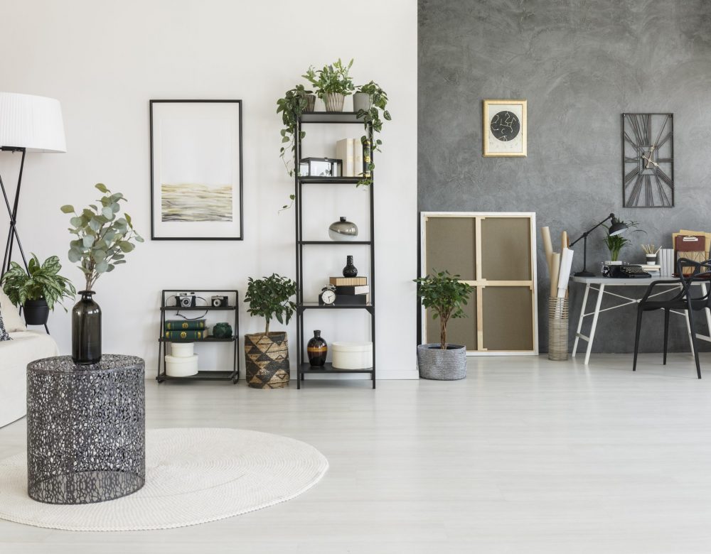 Vase on metal table in open space living room with workspace, plants and contrast colors walls