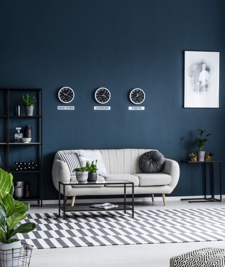 White sofa, coffee table, clocks on the grey wall and striped rug in a modern living room interior