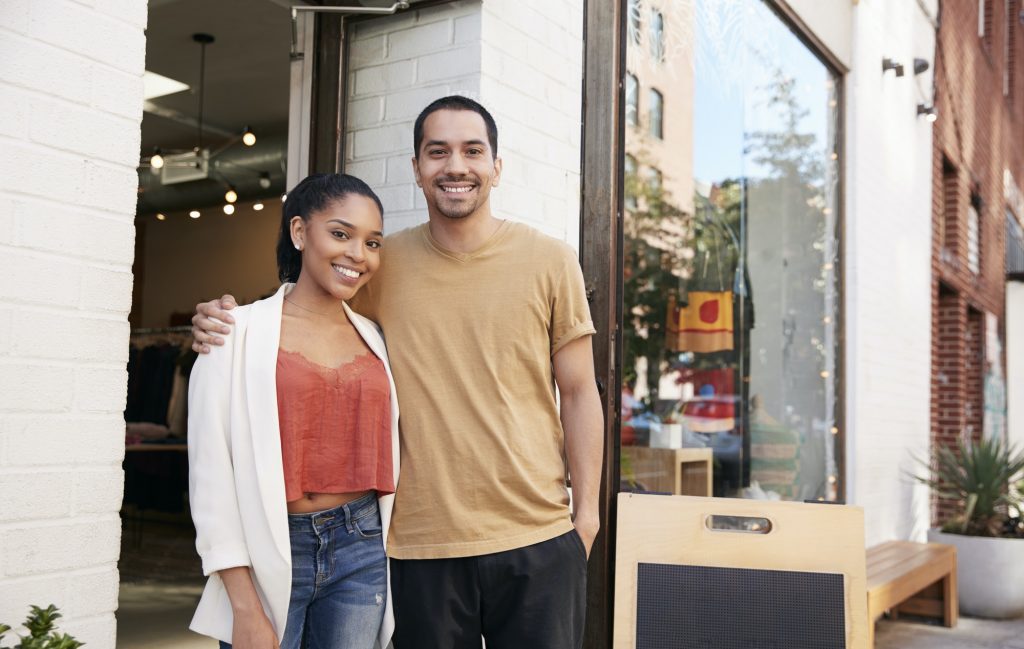 Young Hispanic couple smiling to camera outside their shop